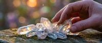 Hand gently touching clear quartz crystals on wooden surface with warm bokeh lights creating magical healing energy atmosphere for wellness meditation.