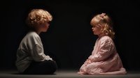 Two adorable toddlers sitting face to face on dark background, boy and girl in casual clothing having intimate conversation moment for family concepts.