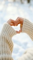 Hands in a cozy knit sweater forming a heart shape against a soft winter sky, symbolizing love, warmth, and romance.