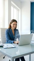 Professional businesswoman in blue suit working on laptop at modern office desk with financial charts and reports for corporate presentations.