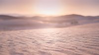 Serene winter landscape with snow-covered field and misty mountains at sunrise, soft golden light creating peaceful atmosphere for nature and seasonal backgrounds.