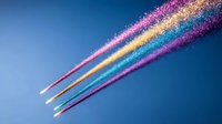 Colorful glowing trails of light streak across dark blue sky creating magical rainbow effect with pink, gold, turquoise and purple sparkles against evening atmosphere.