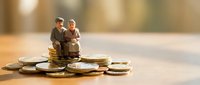 Miniature elderly couple figurines sitting on stacked coins, representing retirement savings, financial planning, and wealth management for senior citizens.