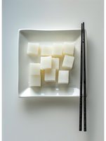 White sugar cubes arranged on square ceramic plate with black chopsticks against light background, minimalist Asian dining presentation for food and beverage styling.