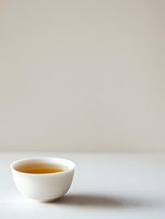 White ceramic bowl filled with golden tea on minimal light background, creating serene composition with negative space for text placement.