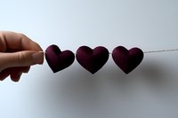 Purple felt hearts hanging on string against white background, minimal romantic composition showing fingers holding decorative Valentine garland.