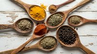 Colorful spices and herbs in wooden spoons arranged on rustic white background. Turmeric, paprika, oregano, black pepper for cooking and seasoning.