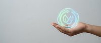 Hand holding a glowing holographic green energy icon with leaf and electric plug, symbolizing sustainable power and eco-friendly technology concepts.