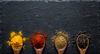 Colorful spices and seasonings arranged in wooden spoons on dark slate background for culinary cooking and food preparation projects.