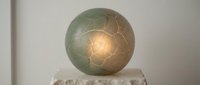 Glowing sphere with geometric pattern on stone pedestal against neutral background, suitable for modern interior design and contemporary art projects.
