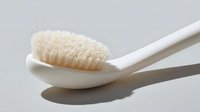 White plastic toothbrush with soft beige bristles casting shadow on light gray background, minimalist dental hygiene concept for healthcare and wellness.