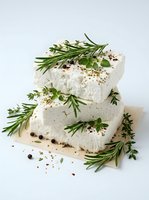 Stacked fresh cheese blocks with rosemary sprigs, peppercorns and herbs on white background, suitable for food styling and culinary publications.
