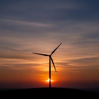Wind turbine silhouette against dramatic sunset sky with orange and purple clouds. Renewable energy concept for sustainable power generation and environmental projects.
