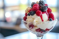 Fresh berries and cream dessert in elegant glass with layers of whipped cream, raspberries, blackberries and blueberries, served on bright background.