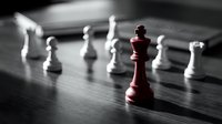 Red chess king stands prominently among white pieces on wooden board, symbolizing leadership, strategy, and standing out from competition in business.