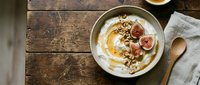 Creamy yogurt bowl topped with fresh figs, granola, and honey drizzle on rustic wooden table with linen napkin and wooden spoon for breakfast or healthy eating content.