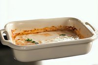 Empty ceramic baking dish with food residue and sauce remnants after serving, showing traces of home-cooked meal on white porcelain cookware.