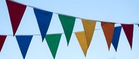 Colorful triangular bunting flags hanging against clear blue sky for festive celebrations, parties, outdoor events and holiday decorations.