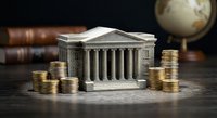 Miniature bank building with classical columns surrounded by golden coin stacks on wooden desk with vintage books and globe in background.