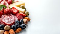 Gourmet charcuterie board with fresh strawberries, blueberries, salami, cheese, olives, nuts and mint leaves on white background for elegant entertaining.