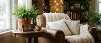 Cozy living room corner with leather armchair, knit throw, white pillows, fern plant, and warm fairy lights creating a hygge atmosphere.