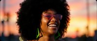 Happy young African American woman with afro hairstyle and sunglasses smiling at sunset. Joyful portrait with warm golden hour lighting for lifestyle content.