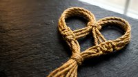 Handmade rope heart shape on dark wooden surface symbolizing love, connection and rustic romance for Valentine's Day or wedding decorations.