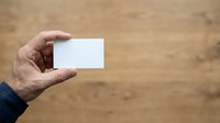 Male hand holding blank white business card against wooden background for branding and corporate identity mockup purposes.