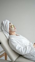 Woman relaxing in white bathrobe with facial mask and cucumber slices on eyes during spa treatment at wellness center for skincare routine.