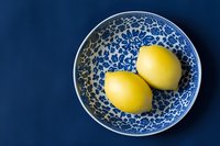 Two fresh yellow lemons in a blue and white floral ceramic plate on a deep navy blue background, top view, minimalist food styling.