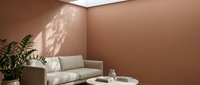 Warm terracotta corner room with cream sofa, potted fern, round white table, and natural light casting shadows on walls for modern interior design.