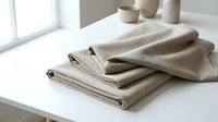 Stack of folded beige linen fabric on white table with ceramic bowls in bright minimalist interior for home textile and sewing projects.