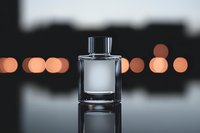 Elegant glass perfume bottle on reflective surface with blurred bokeh lights in background creating luxurious atmosphere for cosmetic and fragrance marketing.