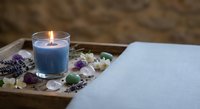 Relaxing spa setup with blue candle, lavender, crystals and flowers on wooden tray creating peaceful wellness atmosphere for meditation and self-care rituals.