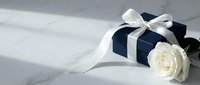 Elegant navy blue gift box with white satin ribbon bow and white rose on marble surface, soft natural light, luxury present for special occasions.