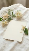 Blank cream card with delicate white flowers and green foliage arranged on natural linen fabric, perfect for wedding invitations, greeting cards, and stationery design projects.