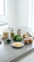 Healthy breakfast ingredients arranged on kitchen counter with oats, nuts, honey, spinach and sliced banana for nutritious morning meal preparation.