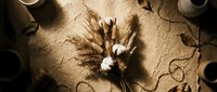Autumn wheat ears with cotton flowers arranged on textured beige surface surrounded by ceramic cups creating cozy seasonal flat lay composition.