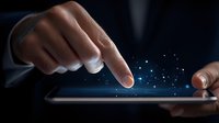 Male hands touching digital tablet screen with glowing blue particles effect, demonstrating modern technology interaction in dark business setting.