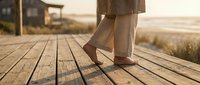 Woman walking on wooden boardwalk during golden hour sunset with ocean view. Relaxing coastal lifestyle and peaceful vacation moments by the sea.