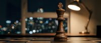 Wooden chess queen piece on board with blurred city lights and desk lamp in background, representing strategy, leadership, and business decision-making.