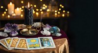 Mystical tarot reading setup with crystals, candles and cards on golden cloth creating atmospheric fortune telling scene for spiritual guidance and divination practices.