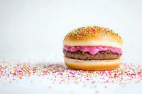 Colorful burger with pink sauce and rainbow sprinkles on white background. Creative food concept with festive candy decoration and sesame seed bun.