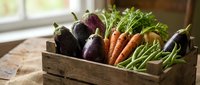 Fresh organic vegetables including eggplants, carrots and leafy greens arranged in rustic wooden crate on kitchen counter for healthy cooking and farm-to-table meals.
