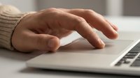 Close-up of professional hand typing on modern laptop trackpad in office environment for business technology and digital workflow concepts.