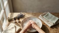 Hands washing in ceramic bowl with dried lavender and natural soap on rustic wooden table creating peaceful spa atmosphere for relaxation and self-care.
