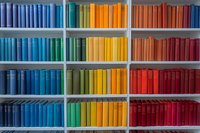 Colorful rainbow bookshelf with books arranged by color spectrum from blue to red, creating vibrant gradient display in modern library or bookstore.