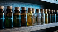 Assorted glass bottles with cork stoppers containing various essential oils and herbal extracts arranged in a row on wooden shelf for aromatherapy, wellness, and natural medicine applications.