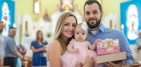 Young family with toddler daughter opening gift box in church interior during celebration event. Parents and child enjoying festive moment together indoors.