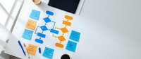 Colorful sticky notes and flowchart diagram on white desk with tablet and pen for business planning, brainstorming sessions and project management workflows.